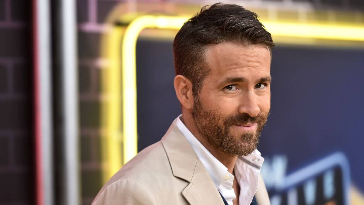 Ryan Reynolds dalam setelan jas berwarna krem, tersenyum menghadap kamera